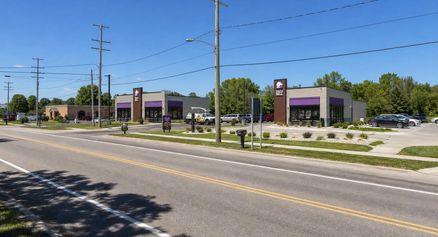 Two purple-trimmed fast-food restaurants stand across from each other beside a multi-lane road.